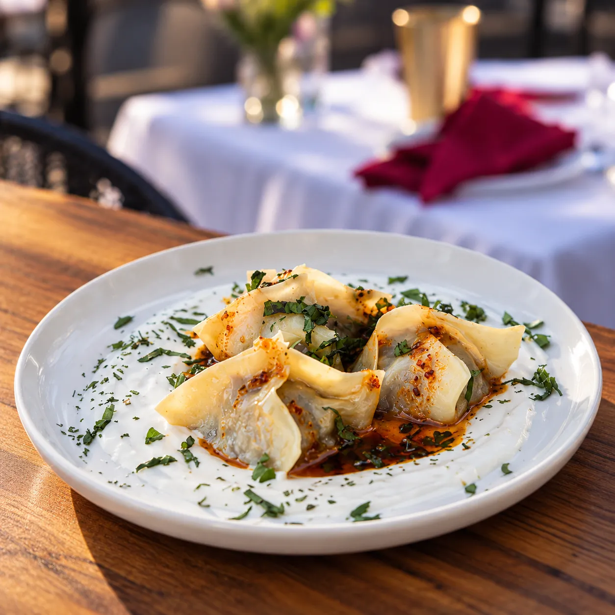 Crispy dumplings over whipped yogurt with chili oil and fresh herbs, served outdoors